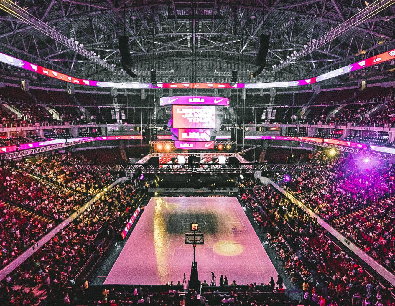 Picture of a full basket ball stadium lit with purple and pink lights